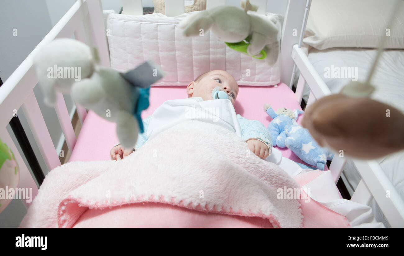 Awake four month baby boy lying in white cot with mobile. Overhead view Stock Photo