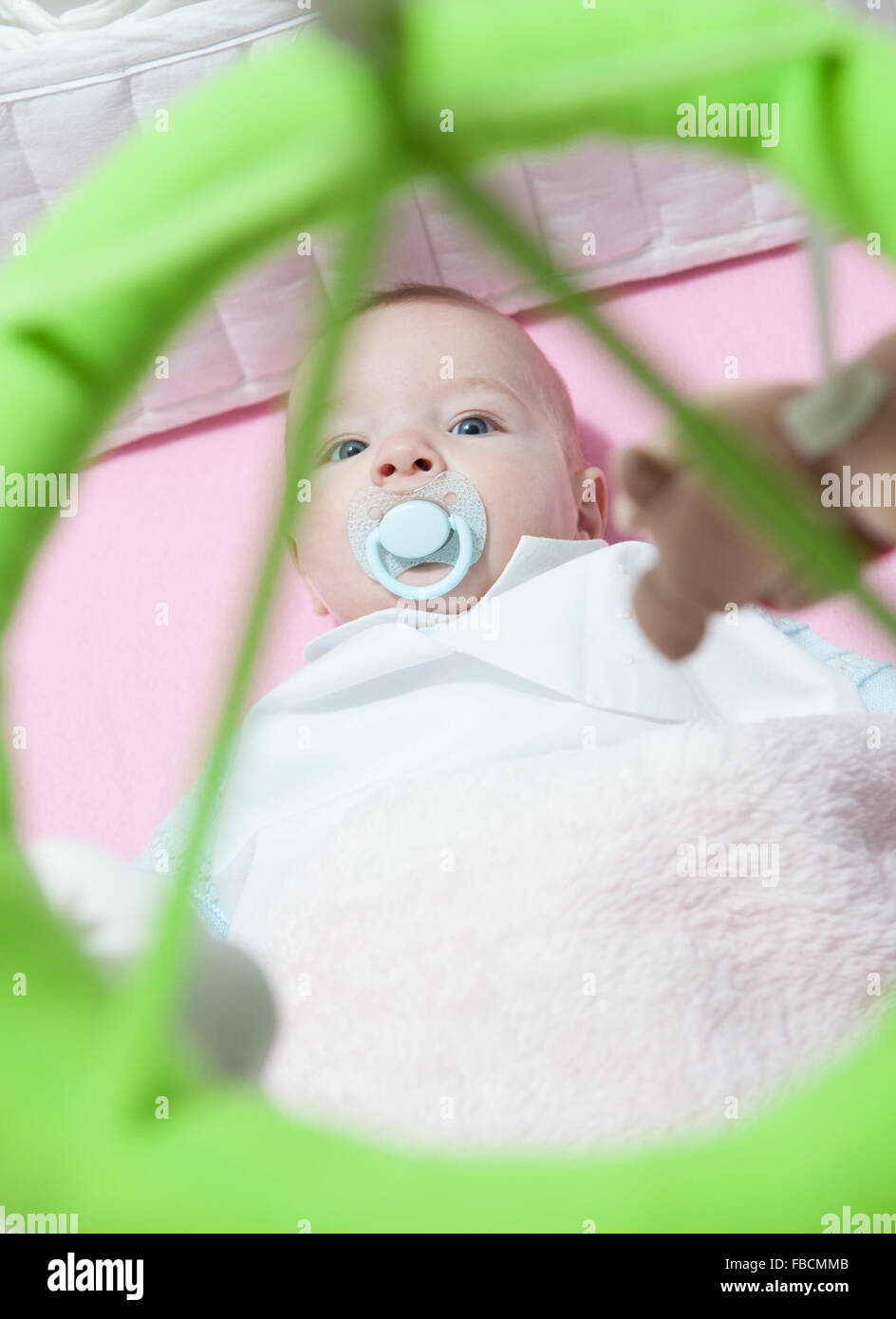Awake four month baby boy lying in white cot with mobile. Overhead view