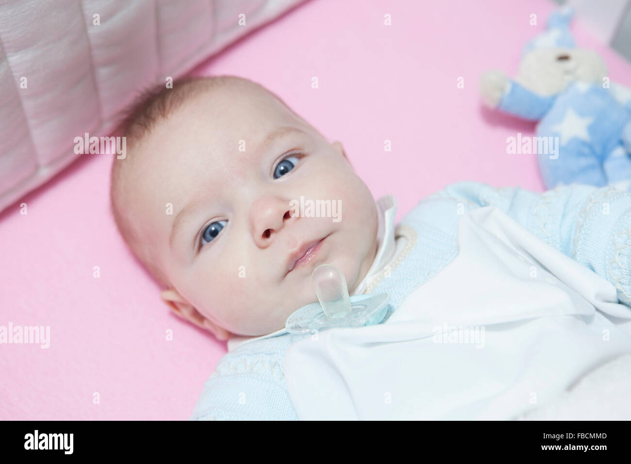 Awake four month baby boy lying in cot with dummy out. Overhead view Stock Photo