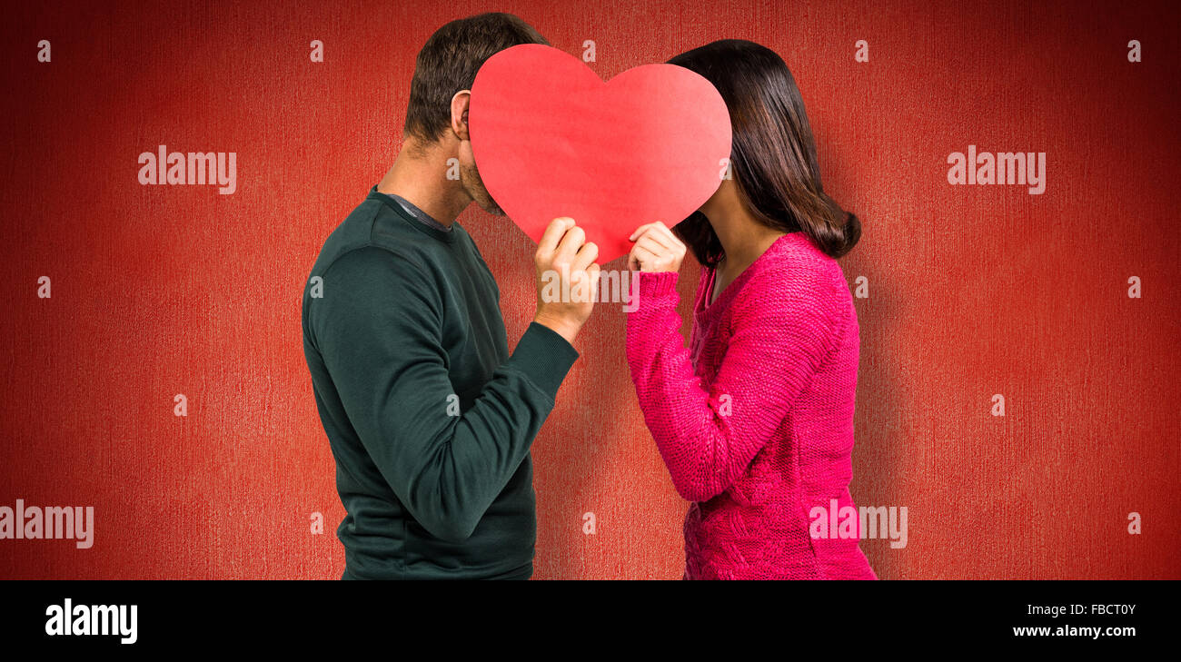 Composite image of couple covering faces with heart shape Stock Photo