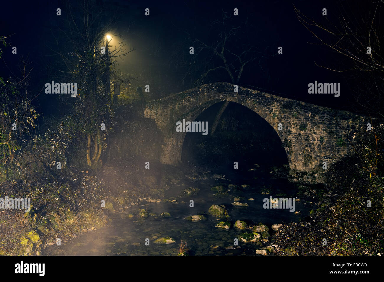 Old stone bridge and light, by night with mist. Stock Photo