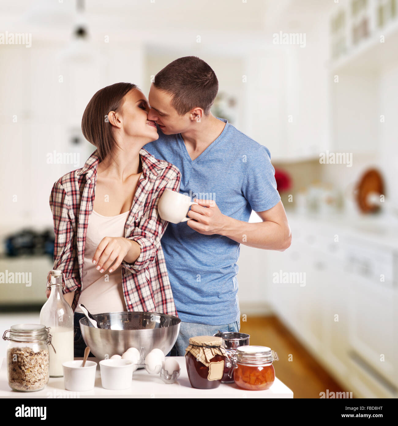 Affectionate man kissing his girlfriend while cutting bread for breakfast in the kitchen Stock Photo