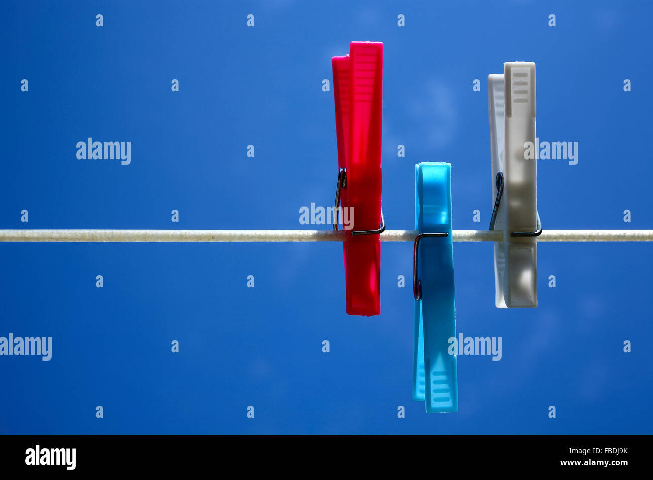 Red blue and white clothes pegs clipped on a washing line with a blue