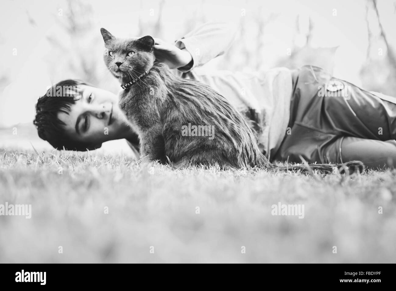 Boy Lying Down On Grassy Field With Cat Stock Photo