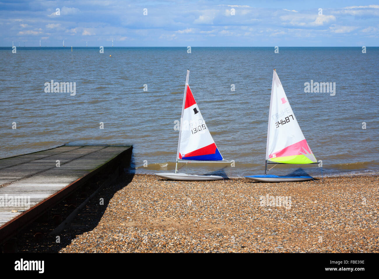 A pair of unoccupied windsurfing boards, standing at the water's edge at Herne Bay in Kent, next to a wooden slipway with a view Stock Photo