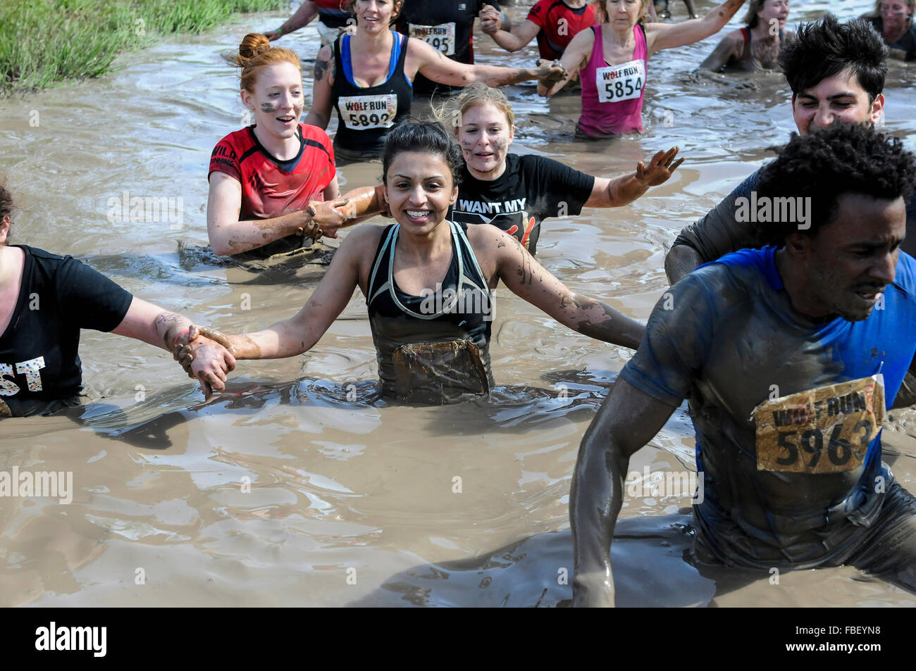 Young female asian runner in mud lake at obstacle course race, UK Stock Photo