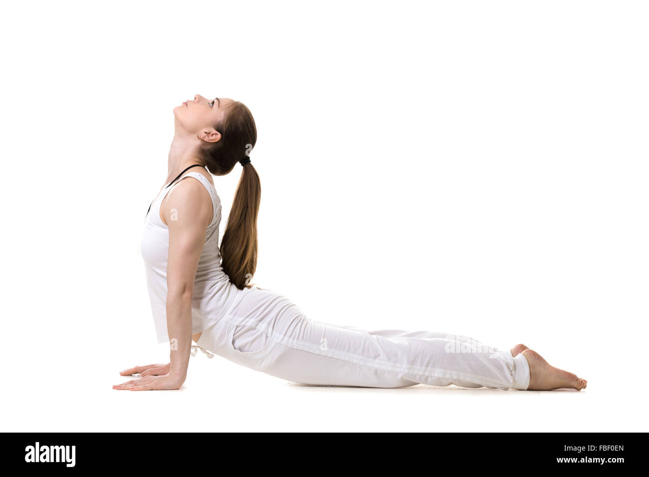 Young fitness model in white sportswear doing yoga or pilates training, urdhva mukha shvanasana (upward facing dog pose), side v Stock Photo