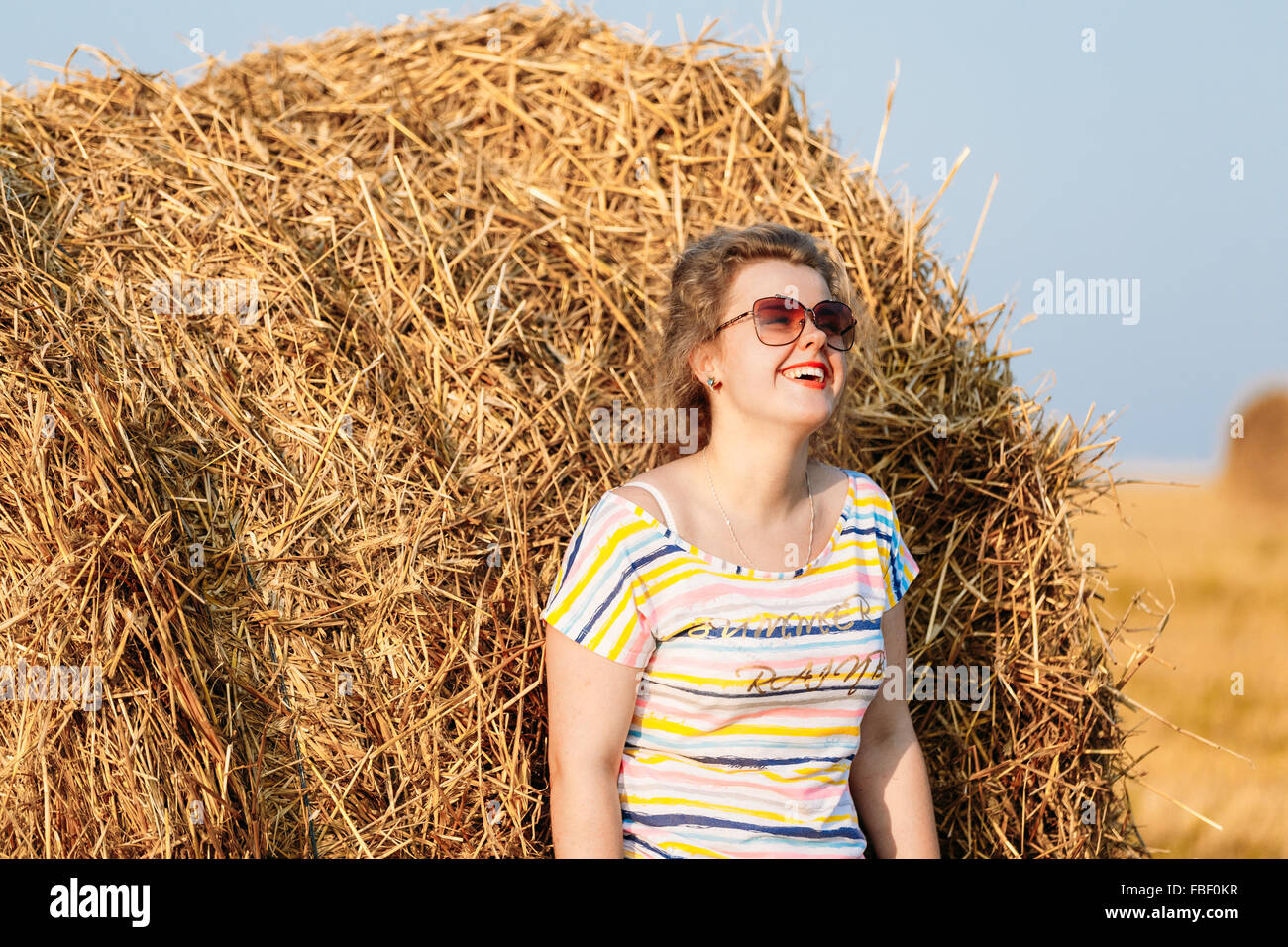 Beautiful Plus Size Young Woman In Shirt Posing In Summer Field Meadow On Hay Bales At Sunset Background Stock Photo
