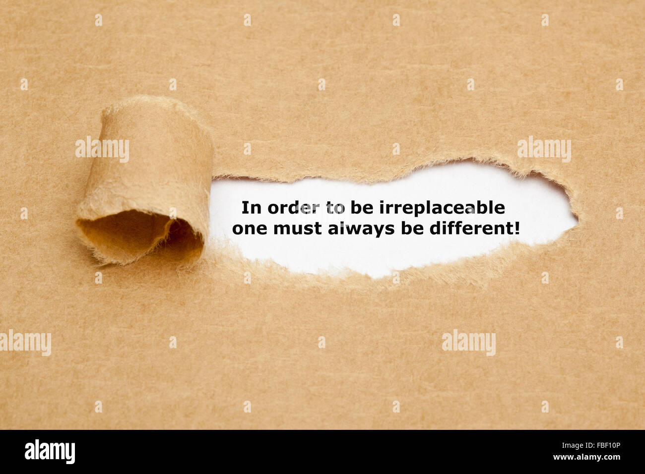 The motivational quote In order to be irreplaceable one must always be different, appearing behind torn paper. Stock Photo