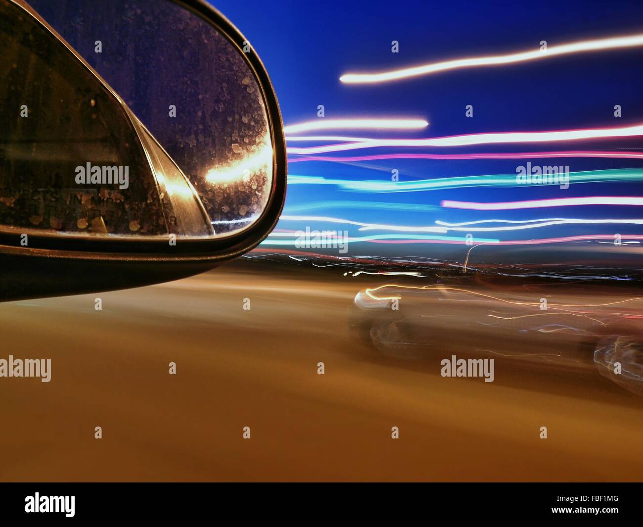 Side-View Mirror And Light Trails On Street At Night Stock Photo