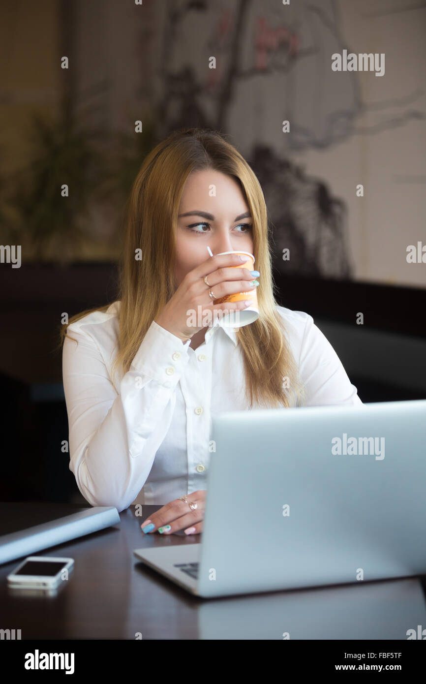 Young beautiful caucasian office woman in formal trendy wear sitting in modern urban cafe tasting her beverage, relaxing after w Stock Photo