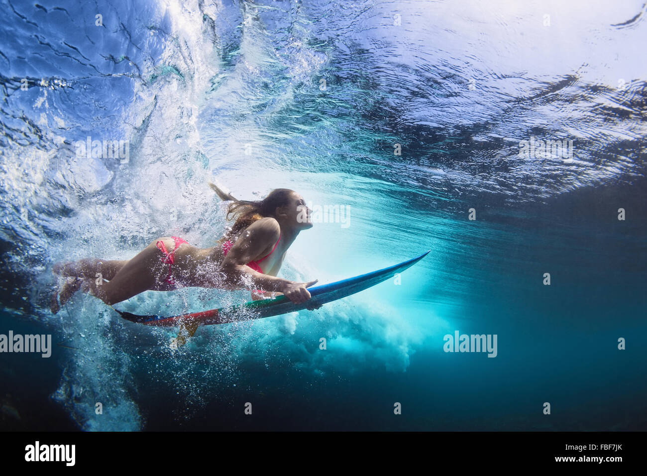 Young girl in bikini - surfer with surf board dive underwater with fun under big ocean wave. Stock Photo