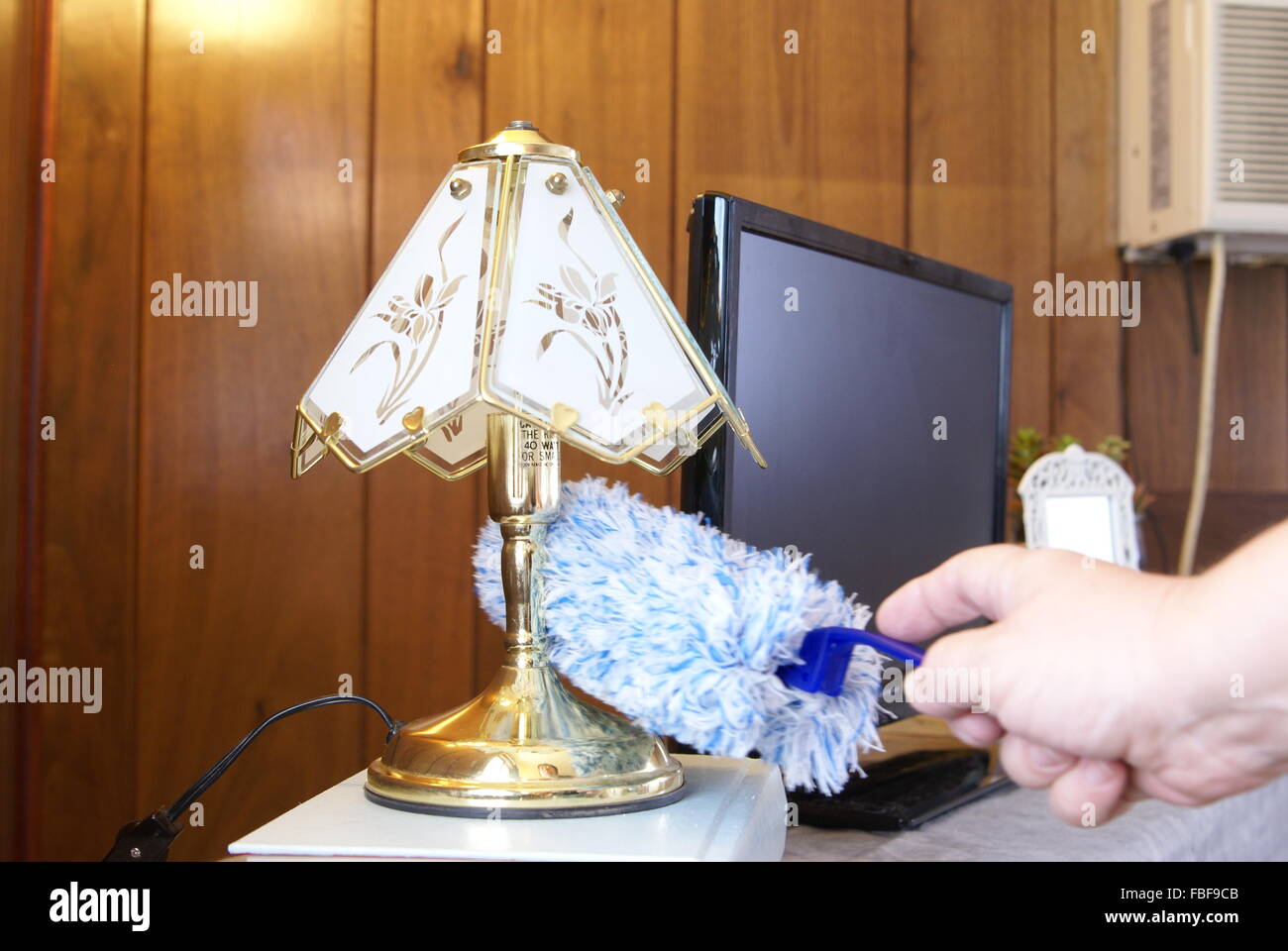 Feather dusting a small table lamp. Stock Photo