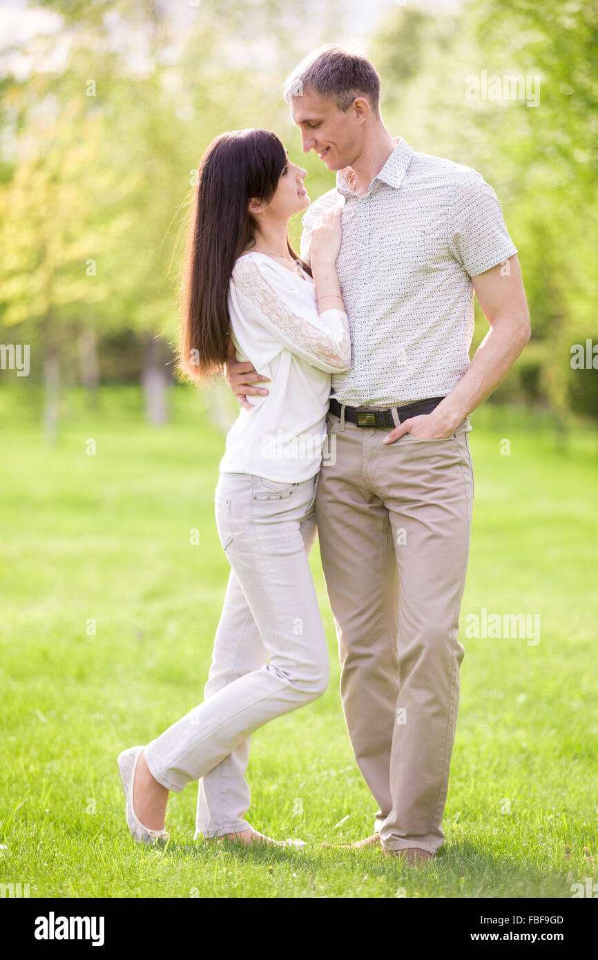Full length portrait of young man and woman on date in park, talking to each other, girlfriend leaning on her boyfriend Stock Photo