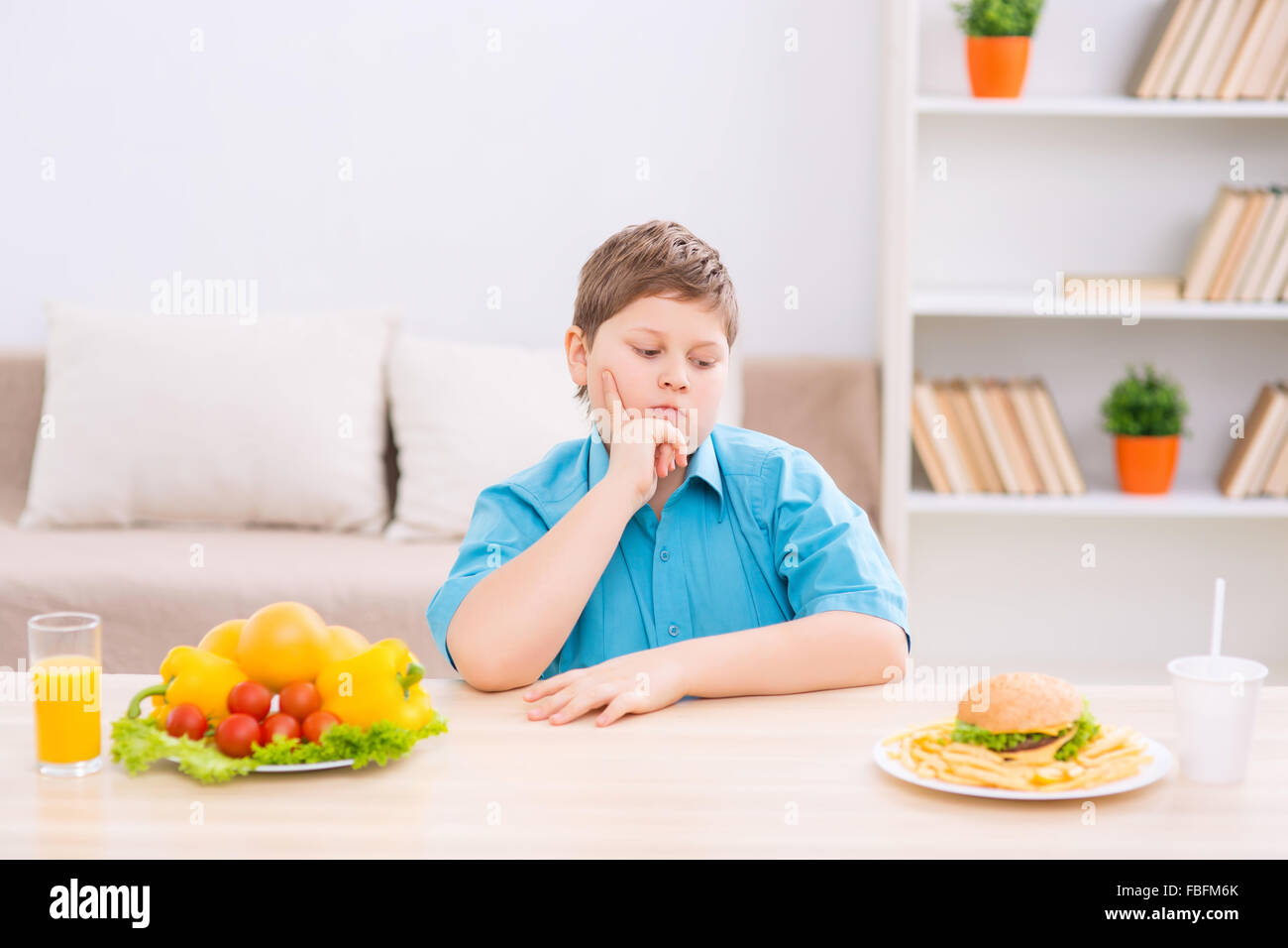 Chubby kid choosing food at the table. Stock Photo