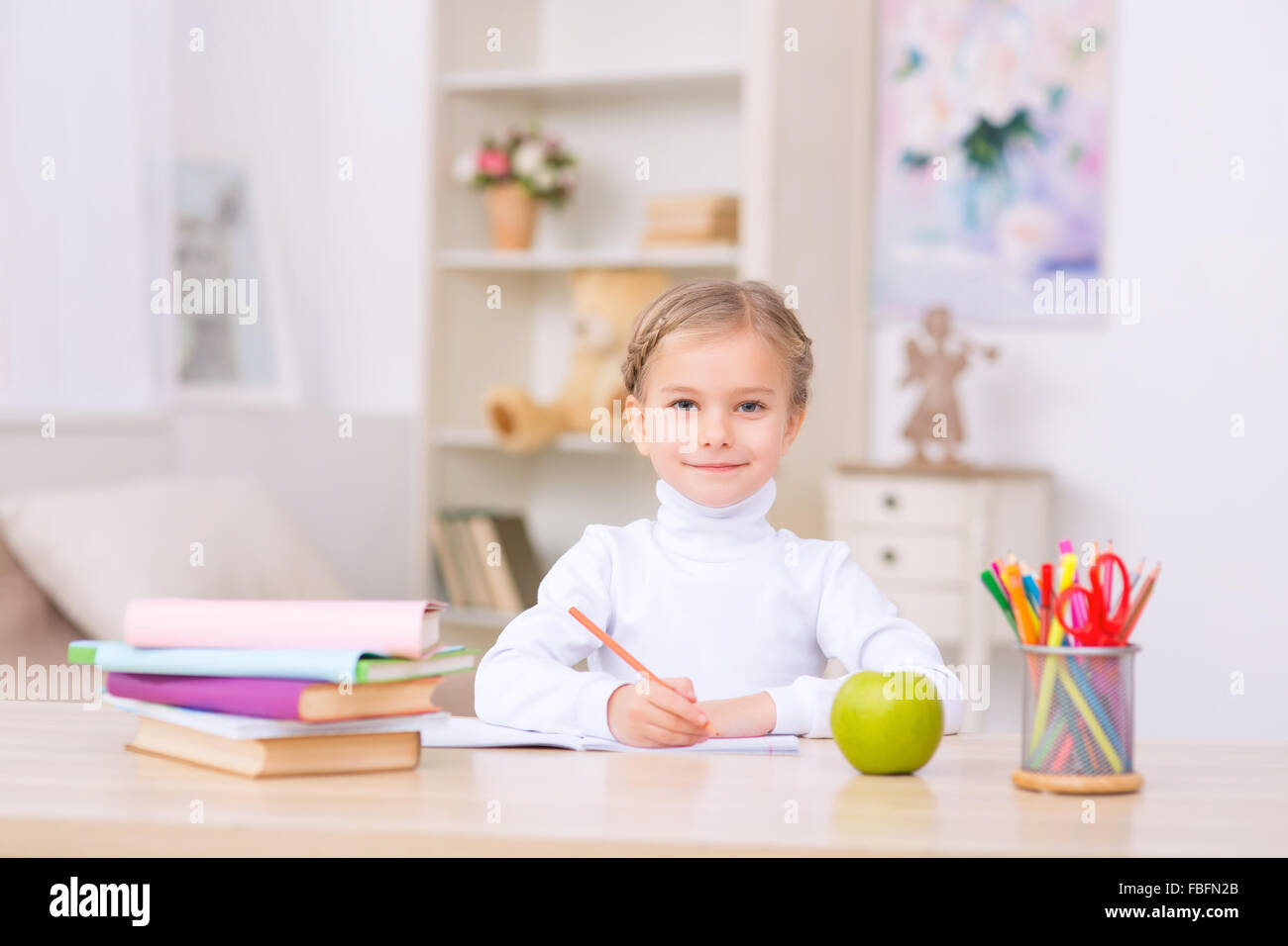 Little girl is sitting at the desk and doing homework. Stock Photo