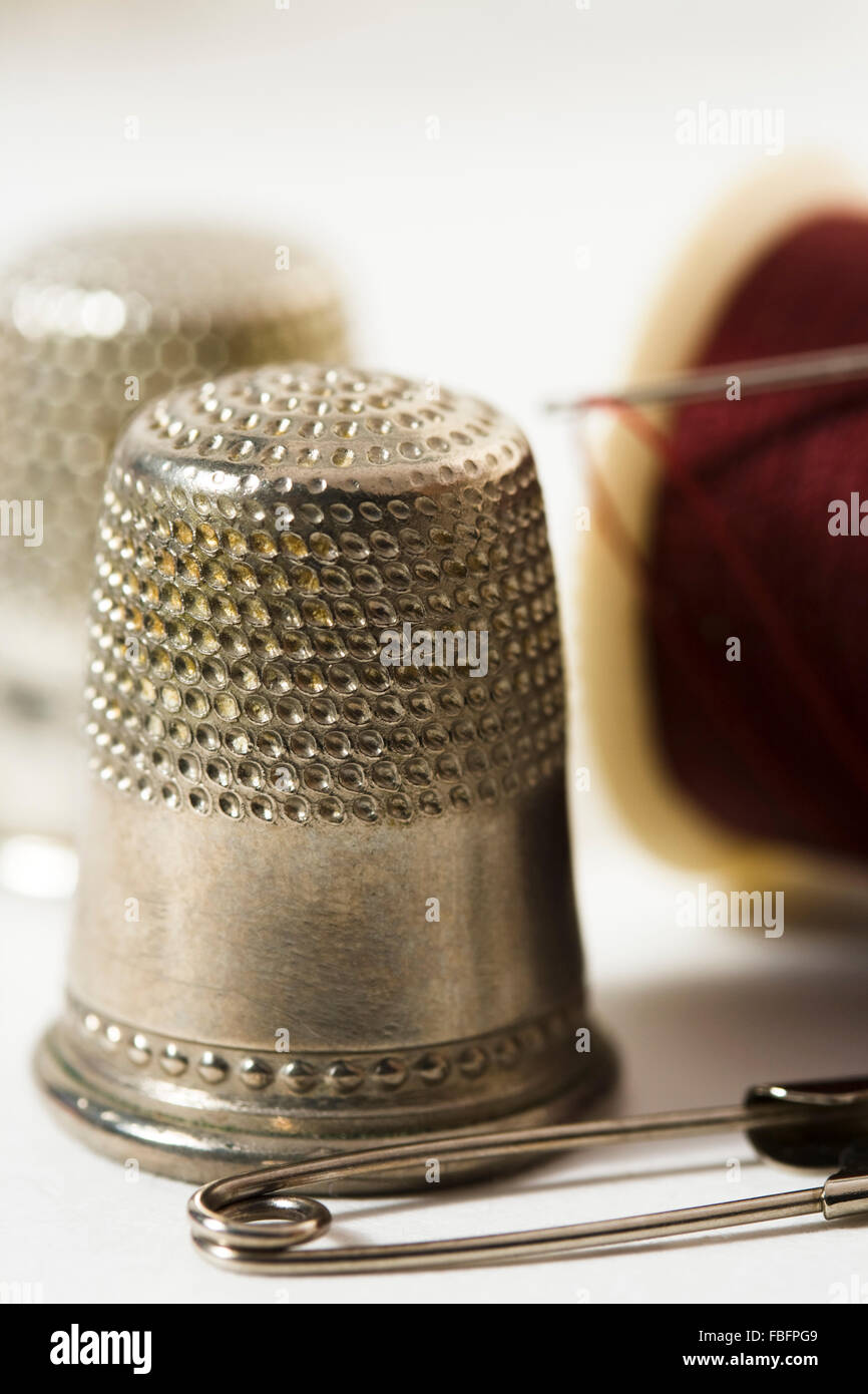 Antique thimbles, needle, dark red thread and pin Stock Photo