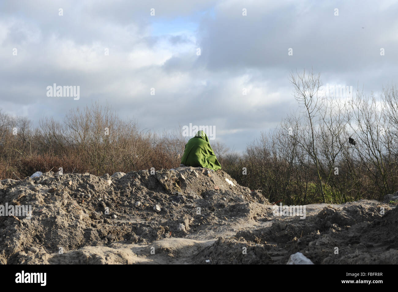 Jungle, Calais, France. A refugees sits in isolation wrapped in a green blanket looking over the