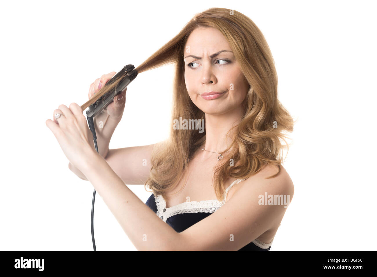 Funny frowning young attractive blond woman holding hair straightener, in bad mood because of her hairstyle, studio isolated por Stock Photo