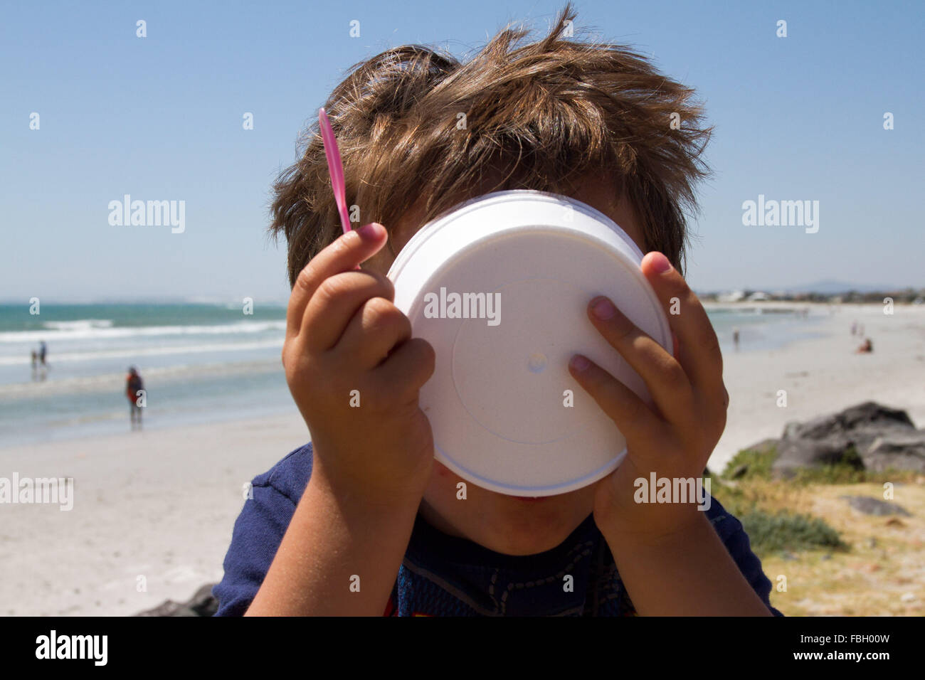 Toddler boy licking out an empty ice cream container. Stock Photo
