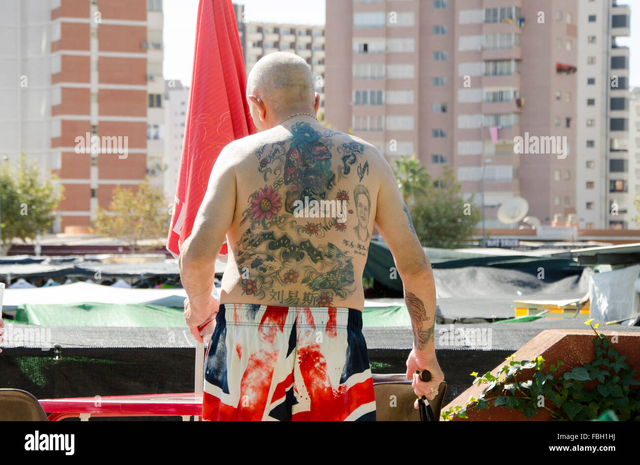British tourist baring his tattooed upper body in shorts decorated with the Union Jack on a weekly market in Benidorm, Alicante, Stock Photo
