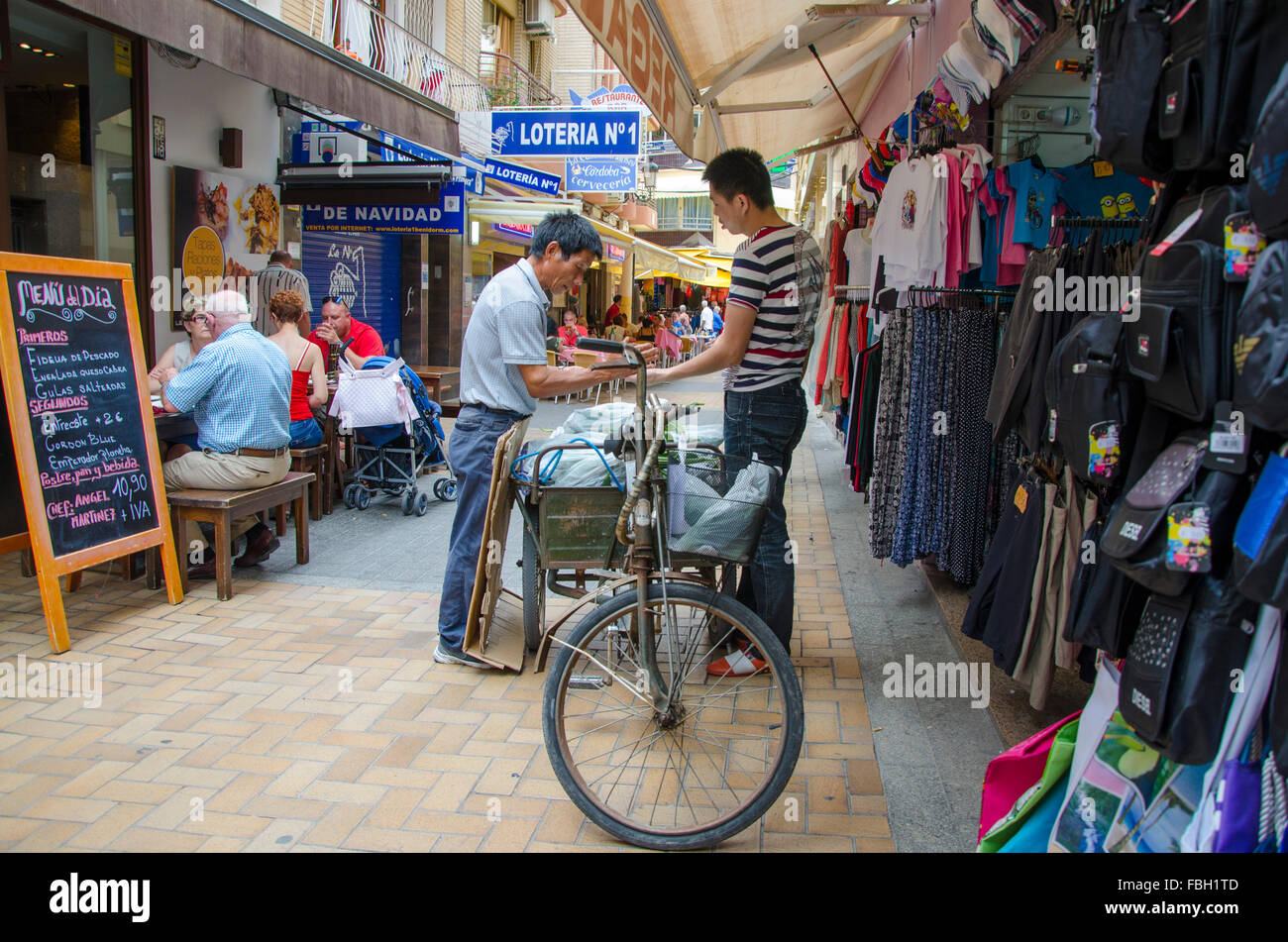 Asian man sells vegetables from his bicycle to another Asian in the pedestrian area of Benidorm, Alicante, Spain Stock Photo