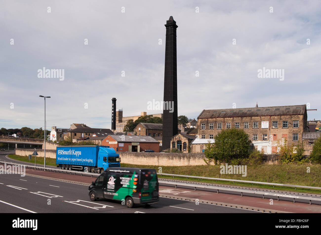 View across vehicles on A650 Bingley Relief Road towards historic, tall, black chimneys of 2