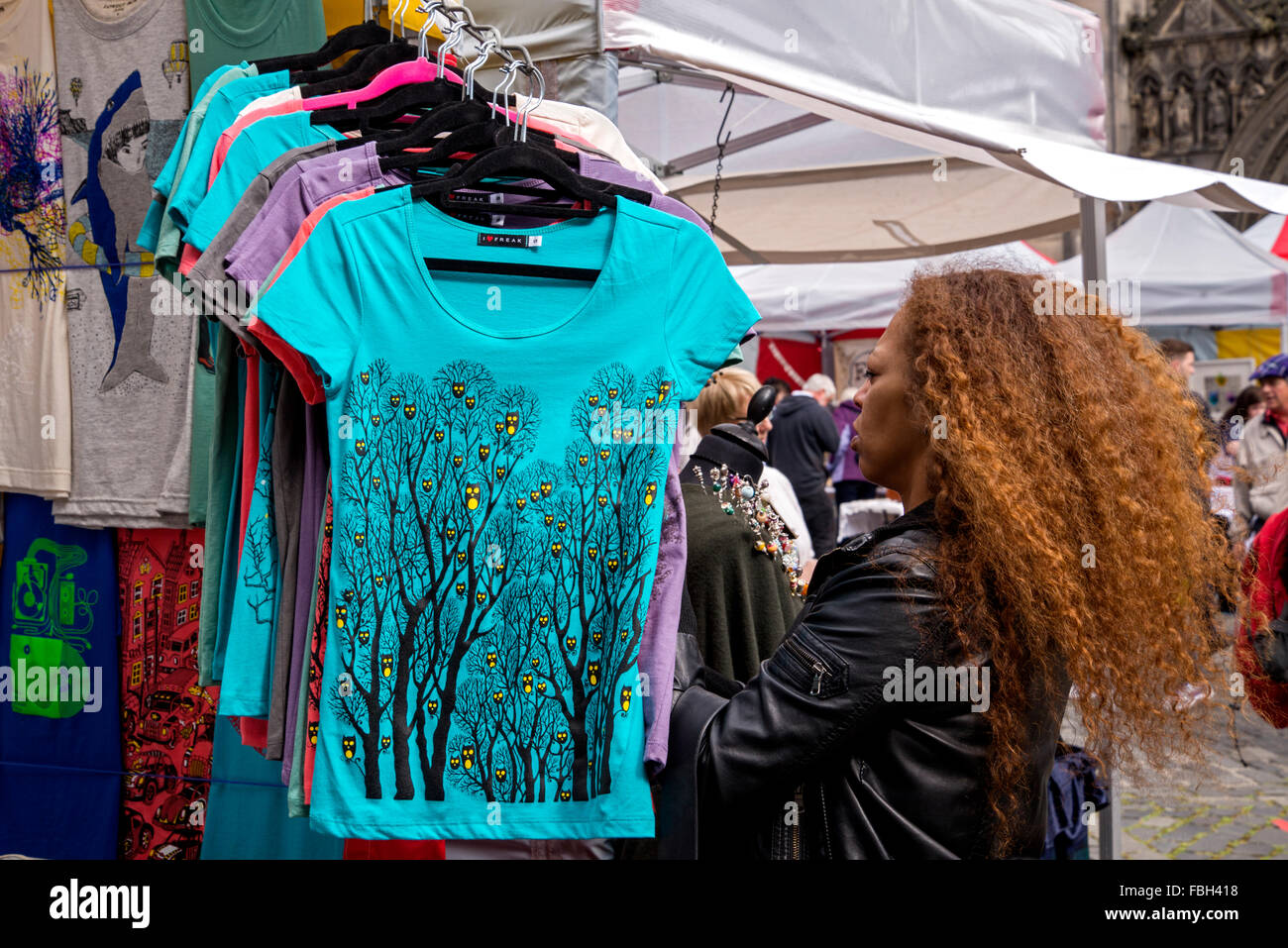 A coloured woman with red hair examines t tee shirts on a stall in Parliament Square during the Edinburgh Festival. Stock Photo