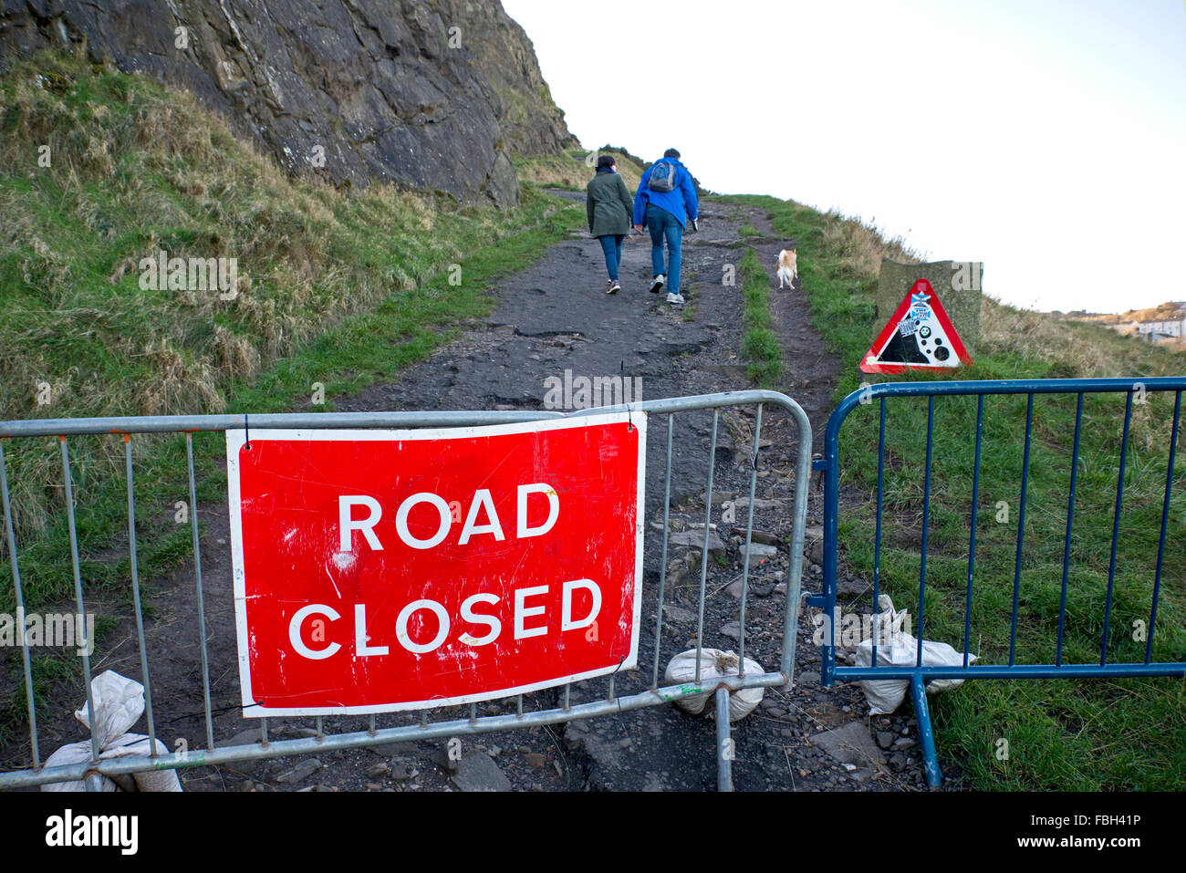 Members of the public ignore the 'Road Closed' sign to walk their dog below Salisbury Crags despite the risk of rock fall. Stock Photo