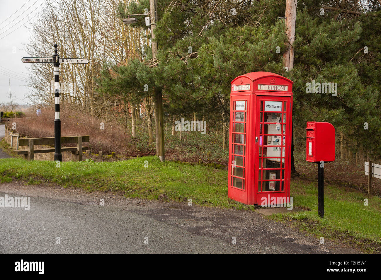 Red telephone box and red post box with finger post road sign at the Cheshire village of Timbersbrooke near Congleton Cheshire Stock Photo
