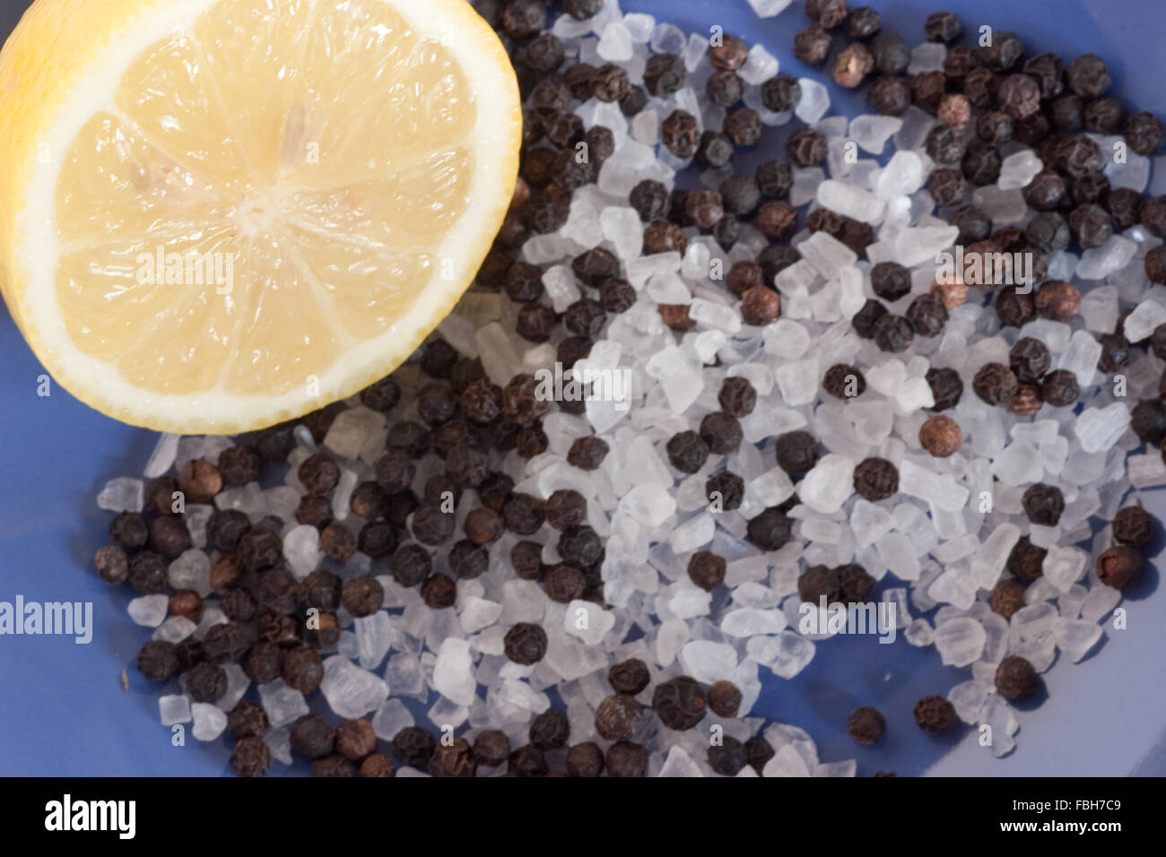 Lemon cut in half with sea salt and black peppercorns on a blue background Stock Photo