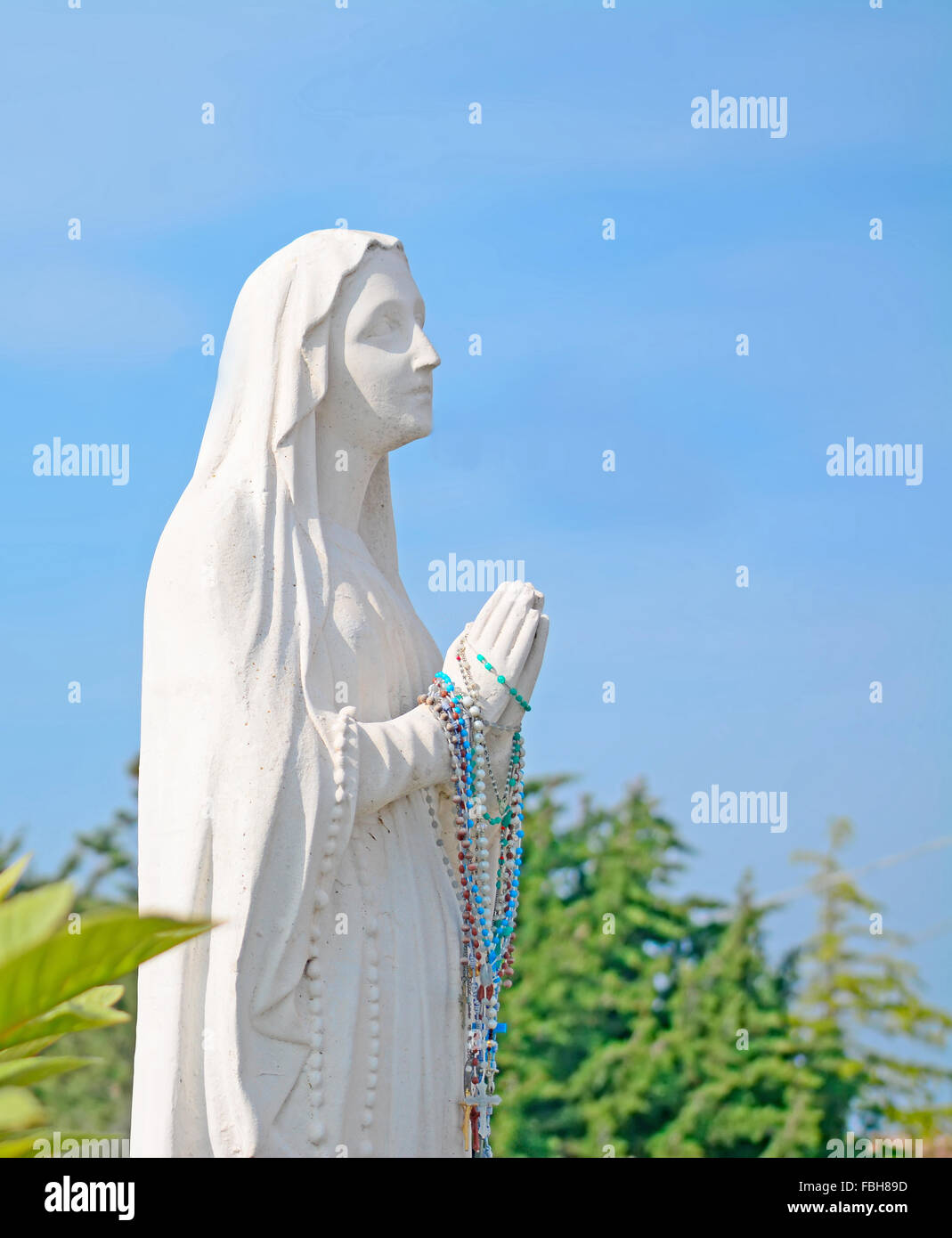 Holy Virgin Mary statue praying under a blue sky Stock Photo - Alamy
