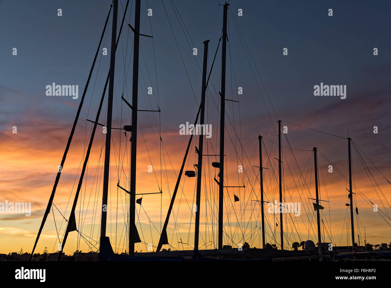 Silhouettes of masts at sunset in the harbor of Kos Greece Stock Photo