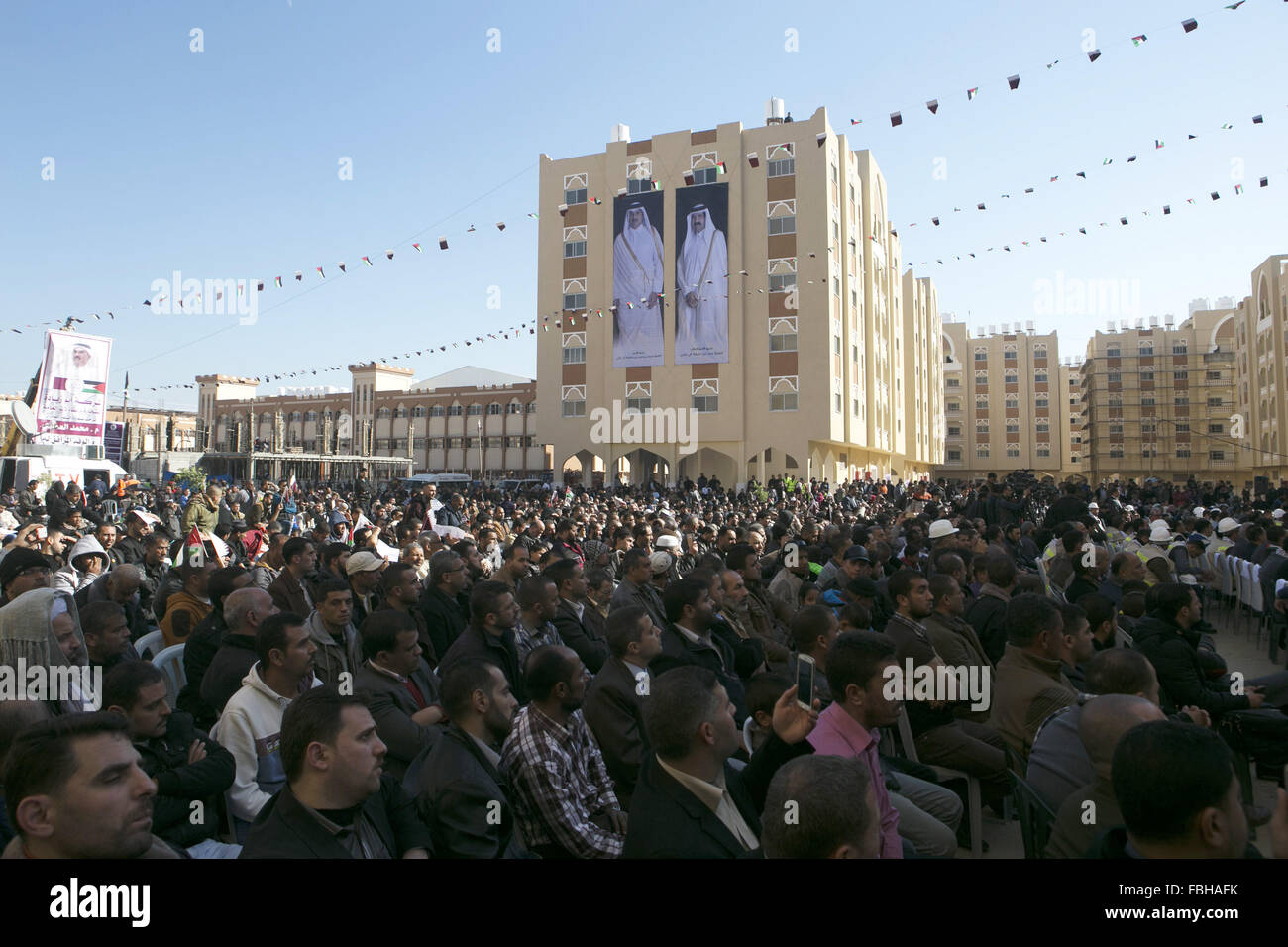 Khan Younis, Gaza Strip, Palestinian Territory. 16th Jan, 2016. Palestinians gather at the Qatari-funded Hamad City housing complex in Khan Younis, southern Gaza Strip, Saturday, Jan. 16, 2016. More than 1,000 Palestinian families have taken possession of new apartments in the first phase of the large housing project that sits on dunes that were part of the former Israeli Jewish settlement of Gush Katif. Huge portraits of former Qatari ruler, Sheik Hamad bin Khalifa Al Thani, right, his son, the current emir, Tamim bin Hamad bin Khalifa Al Thani, and the Qatari flag hang on one of the buildin Stock Photo