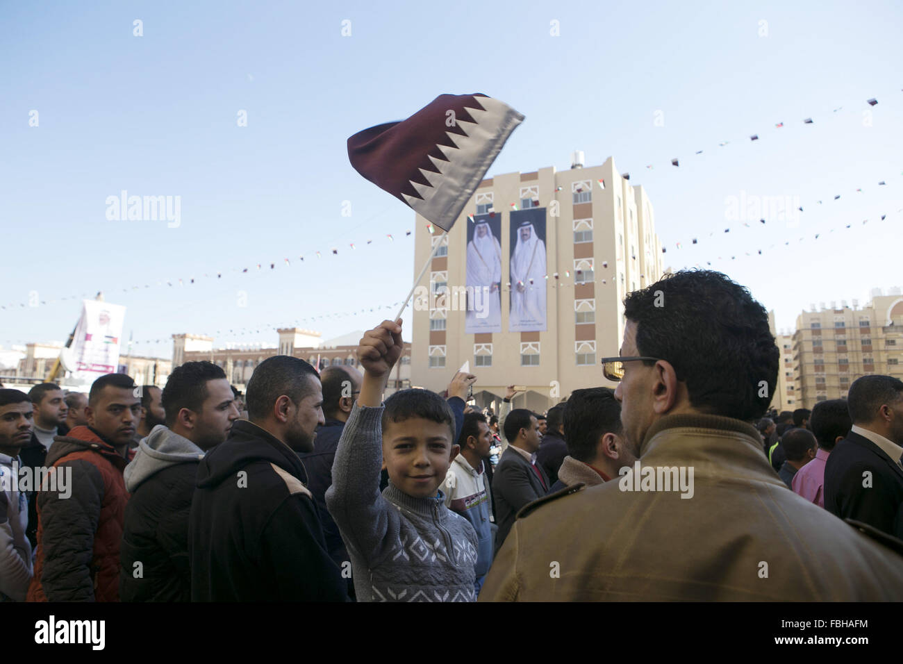 Khan Younis, Gaza Strip, Palestinian Territory. 16th Jan, 2016. Palestinians gather at the Qatari-funded Hamad City housing complex in Khan Younis, southern Gaza Strip, Saturday, Jan. 16, 2016. More than 1,000 Palestinian families have taken possession of new apartments in the first phase of the large housing project that sits on dunes that were part of the former Israeli Jewish settlement of Gush Katif. Huge portraits of former Qatari ruler, Sheik Hamad bin Khalifa Al Thani, right, his son, the current emir, Tamim bin Hamad bin Khalifa Al Thani, and the Qatari flag hang on one of the buildin Stock Photo