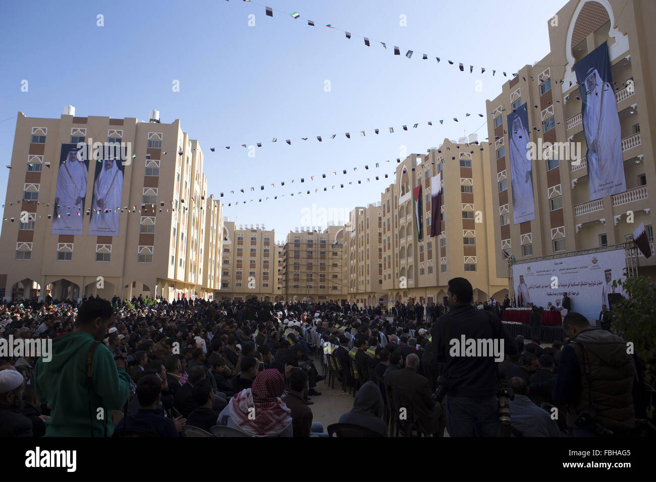 Khan Younis, Gaza Strip, Palestinian Territory. 16th Jan, 2016. Palestinians gather at the Qatari-funded Hamad City housing complex in Khan Younis, southern Gaza Strip, Saturday, Jan. 16, 2016. More than 1,000 Palestinian families have taken possession of new apartments in the first phase of the large housing project that sits on dunes that were part of the former Israeli Jewish settlement of Gush Katif. Huge portraits of former Qatari ruler, Sheik Hamad bin Khalifa Al Thani, right, his son, the current emir, Tamim bin Hamad bin Khalifa Al Thani, and the Qatari flag hang on one of the buildin Stock Photo