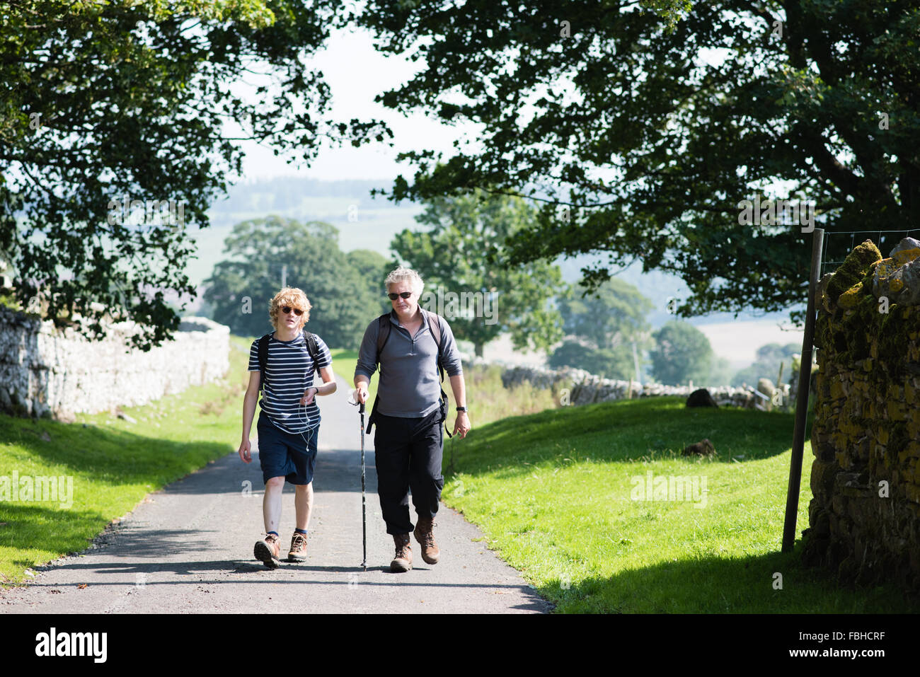 Middle-aged white man and blond-haired white teenage boy hiking in summer along a beautiful country lane near Ullswater in Cumbria, England Stock Photo