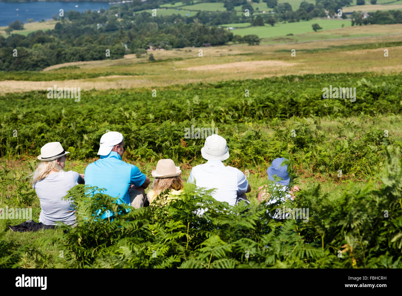 Five white adults sitting in bracken looking across the landscape wearing summer hats enjoying the view towards Ullswater, Cumbria Stock Photo