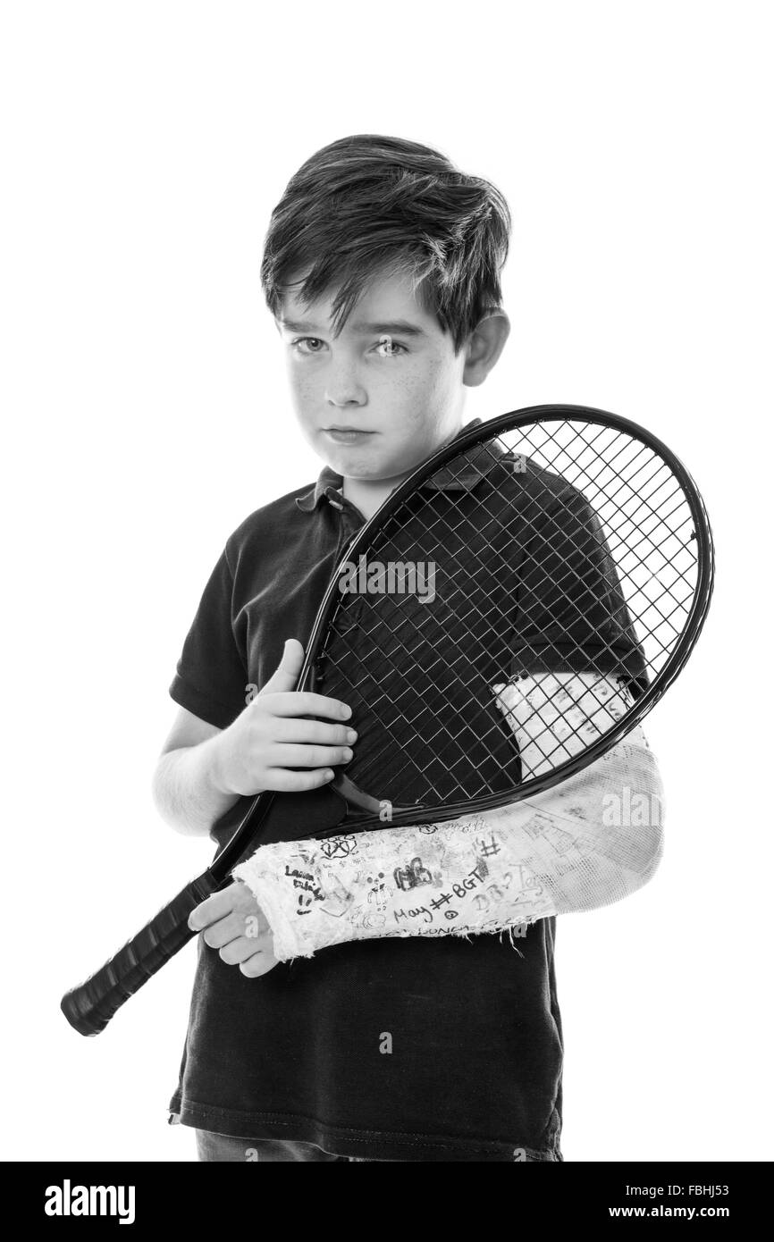 Close up upper body shot of a cute young boy who has broken his left arm and is unhappy because he can't play tennis Stock Photo