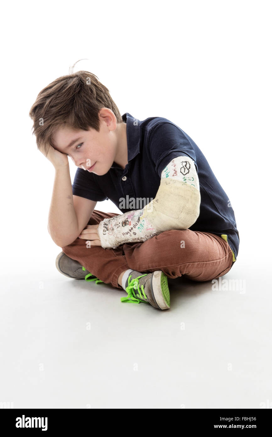 Young boy is sitting down and unable to join in because he has broken his arm Stock Photo