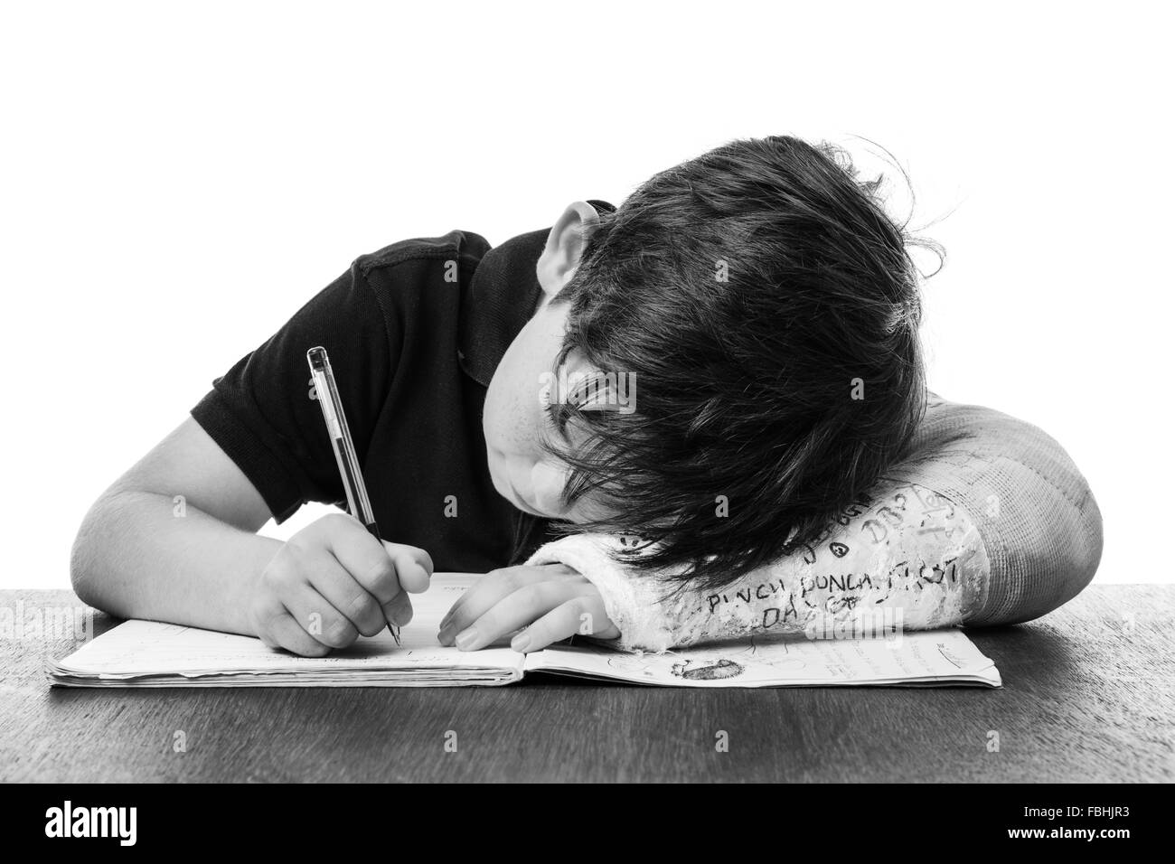 young boy is studying hard, doing his homework, whilst he has a broken left arm Stock Photo