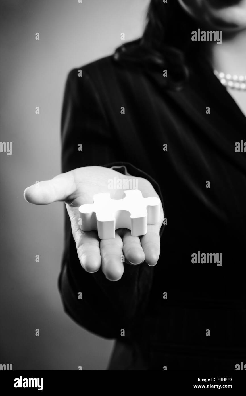 Close up studio shot of a woman holding a 3d puzzle piece in the open palm of her right hand, arm out stretched Stock Photo
