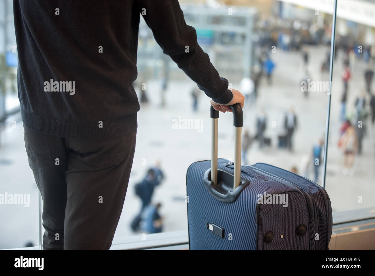 Young handsome man in 20s waiting for flight, standing in modern airport terminal with crowd on background, holding handle of lu Stock Photo