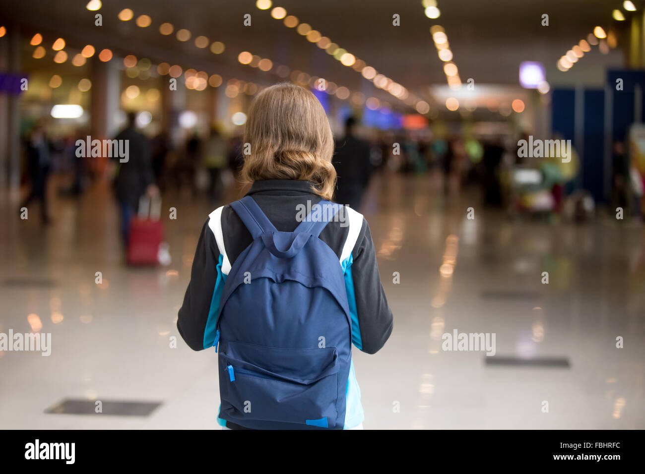 Young woman in 20s with backpack walking in airport terminal, wearing casual style clothes, rear view Stock Photo