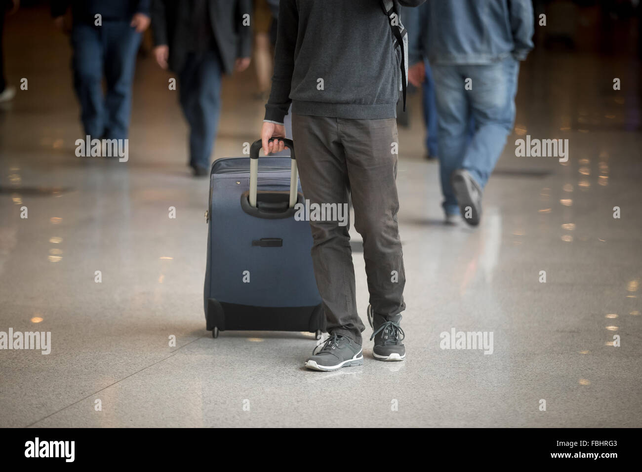 Young man with suitcase walking in modern airport terminal with crowd on background, wearing casual style clothes, close up Stock Photo