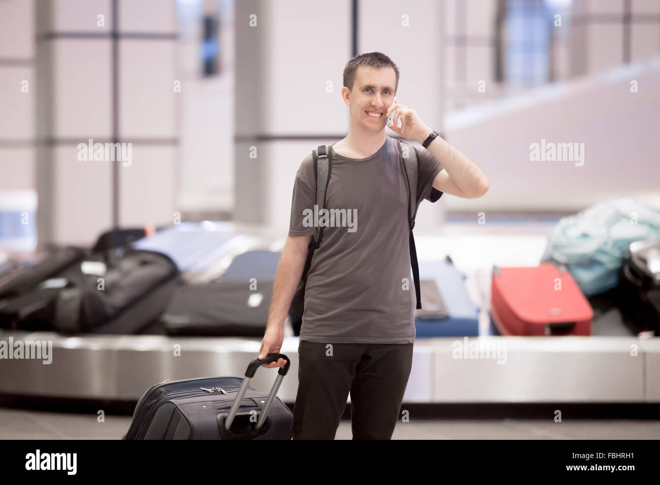 Portrait of young happy smiling handsome traveller man in 20s leaving arrivals lounge of airport terminal building after collect Stock Photo
