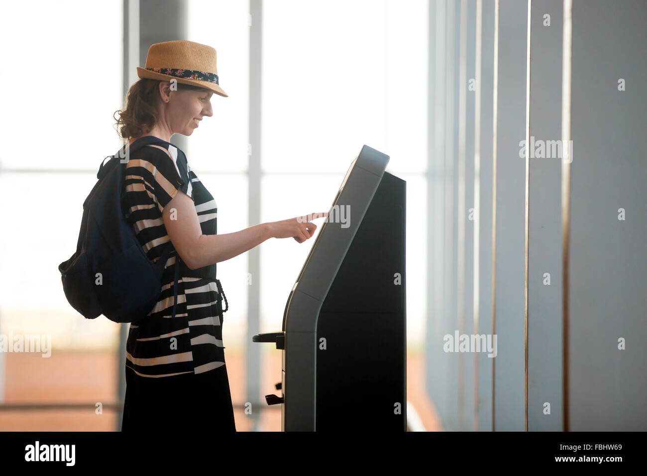 Young woman at self service transfer area doing self-check-in or buying plane tickets at automated machine with touchscreen inte Stock Photo