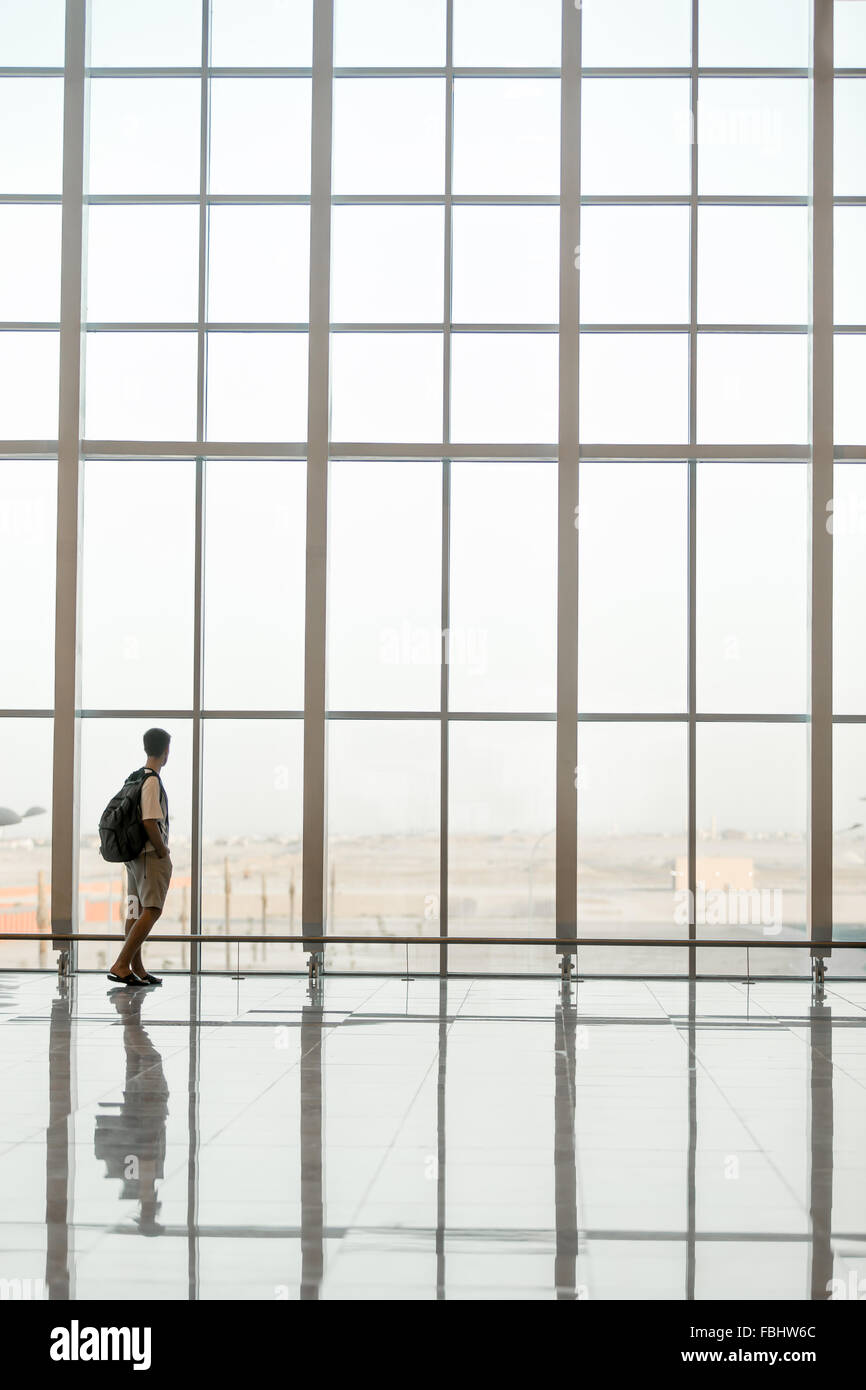 Minimalistic shot of full length silhouette of young handsome man with backpack waiting for flight, standing in modern airport t Stock Photo