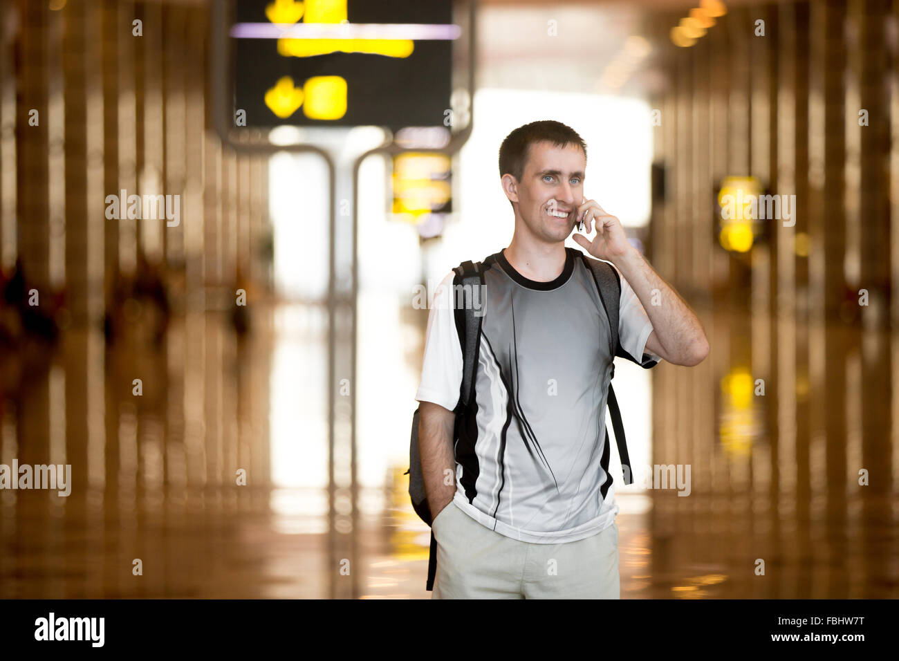 Full length portrait of cheerful, smiling young man with backpack walking in modern airport terminal building, holding cellphone Stock Photo
