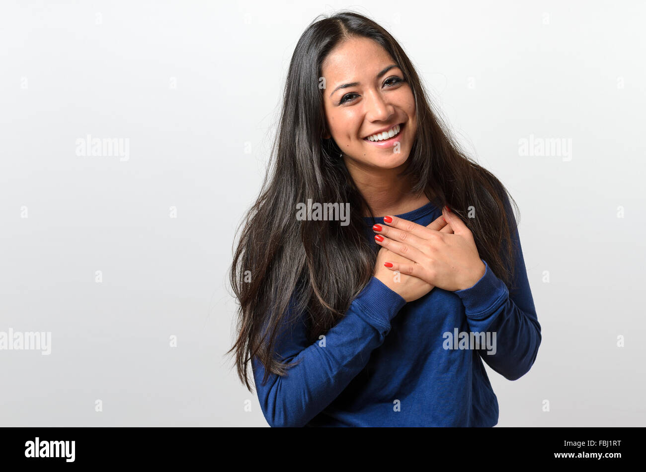 Young woman showing her heartfelt gratitude and thanks clasping her hands to her heart with a pleased smile Stock Photo